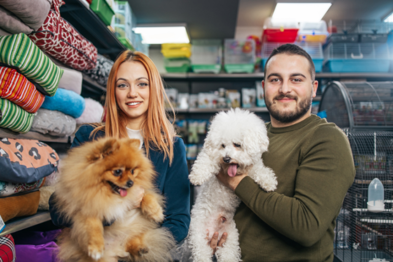 two people standing among shelves of pet products while holding dogs | Letter to the BlogPaws Community: Trade Shows and Our Role as Creators
